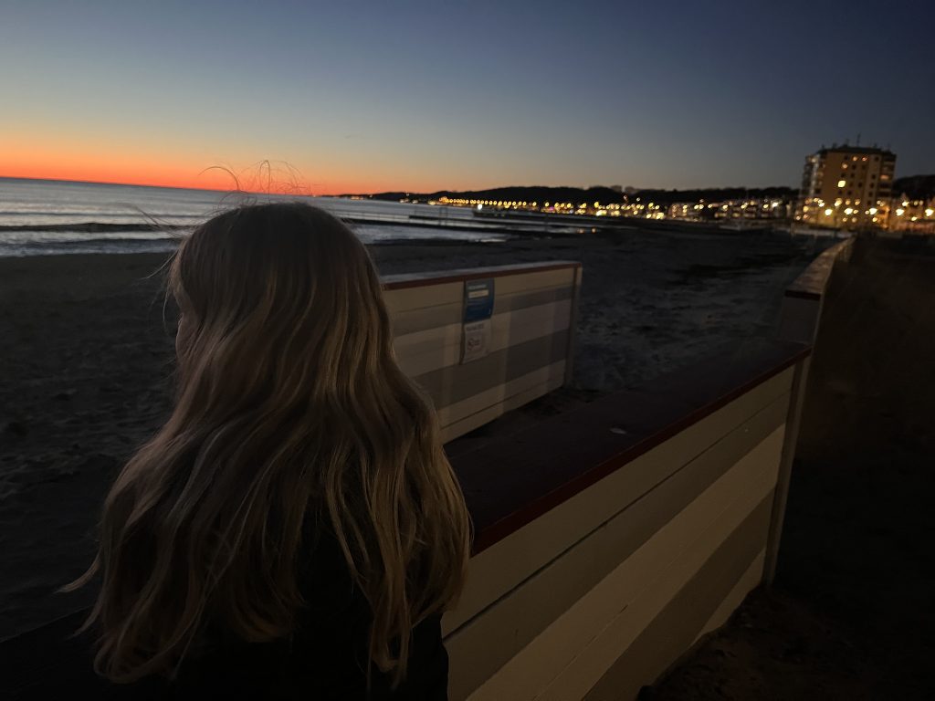 En flicka tittar ut mot havet och solnedgången brinner i horisonten. 